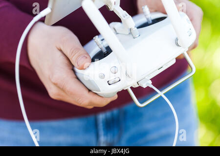 quadcopter flight outdoors, aerial imagery and tech hobby, recreation concept - closeup on pilot hands and white remote radio control, modern high-tech solution for joy flying and video filming. Stock Photo