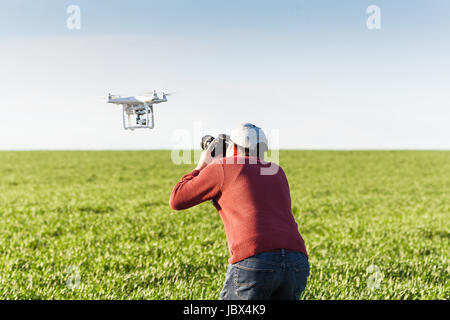quadcopter summer outdoors, aerial imagery and recreation concept - meeting of low-flying drone and professional photographer on summer field of green wheat, blue sky background, mutual photography. Stock Photo