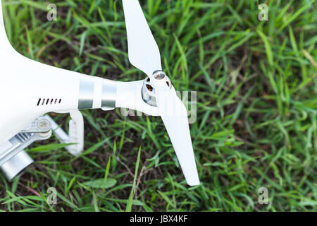 quadcopter outdoors, aerial imagery and tech hobby, recreation concept - rotor of white quadrocopter before flight on summer lawn with green grass, closeup white drone propeller, fuselage and camera. Stock Photo
