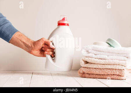 Man's hand putting on the table a jar of gel for washing clothes. Against the background of a pile of towels and soap. Stock Photo