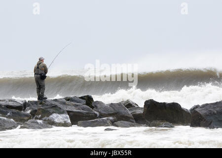 Man fishing from rocks in stormy ocean waves, Long Beach, New York, USA Stock Photo