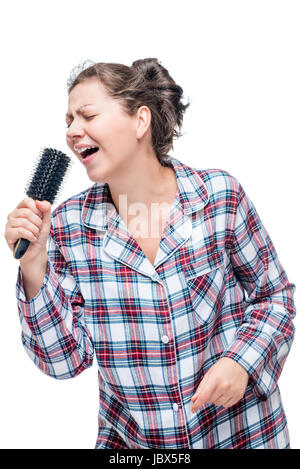 A girl in pajamas loves a song to sing, instead of a microphone a hairbrush on a white background Stock Photo