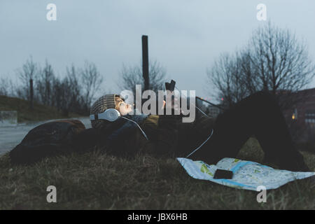 Female backpacker lying in city park at night looking at smartphone Stock Photo