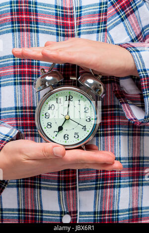 Female hands holding an alarm clock on a background of pajamas close-up Stock Photo