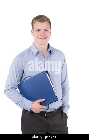 Freigestelltes Foto eines jungen, lächelnden Geschäftsmannes, der einen blauen Aktenorder unter seinem Arm trägt und die andere Hand in seiner Hosentasche hat. Der Mann schaut zur Kamera. Stock Photo