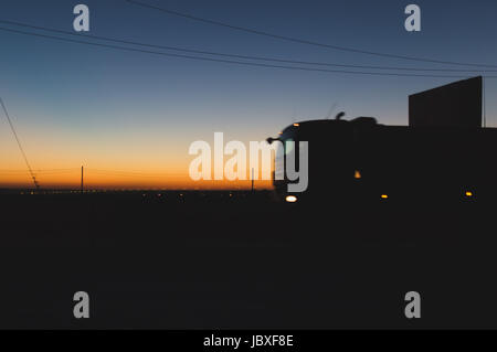 Speeding oncoming trucks with glowing lights on the highway after sunset  Stock Photo