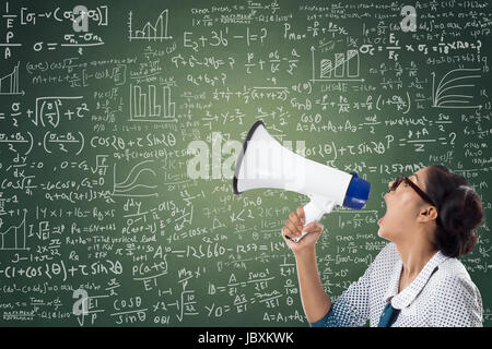 Businesswoman shouting through megaphone against green chalkboard with mathematical formula Stock Photo