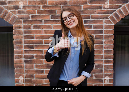 Confident young businesswoman giving the thumbs up against a gray background. Stock Photo