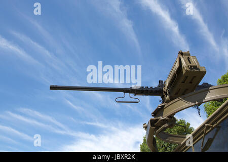 View looking up at a M2 Browning machine gun mounted on a scarff ring on top of a military truck. Blue sky and cloud streaks background. Stock Photo