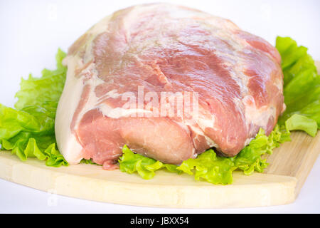 Raw cervical carbonate of pork on cutting board with leaves of green salad, isolated on white background Stock Photo