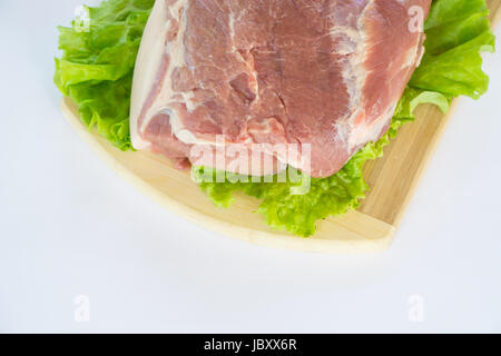 Raw cervical carbonate of pork on cutting board with leaves of green salad, isolated on white background Stock Photo