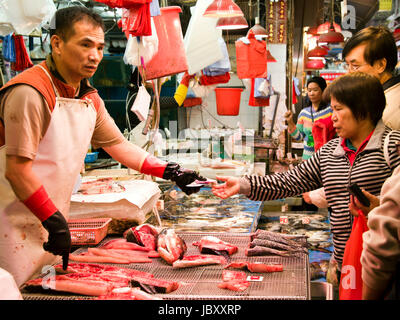 Horizontal view of customers being served at a fishmongers stall at a wet market in Hong Kong, China. Stock Photo