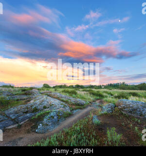 Colorful summer landscape with big stones, green grass, walkway and amazing sky with multicolored clouds at sunset. Nature background. Rocks in the be Stock Photo