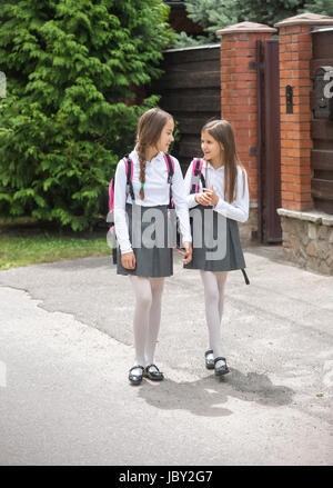 Two cute girls in uniform walking to school and chatting Stock Photo