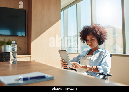 Indoor shot of young african woman sitting in office and using digital tablet. Creative businesswoman using tablet pc. Stock Photo