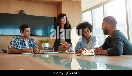 Young businesswoman discussing something with her coworkers while standing at the conference table. Multi ethnic business team meeting in office. Stock Photo