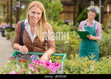 Woman shopping for flowers in garden center employee doing inventory Stock Photo