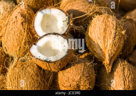 Coconuts, partly broken open, are sold on a busy vegetable market street in the suburb New Market Stock Photo