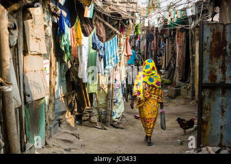 A woman in yellow sari is walking between slum dwellings in Topsia slum Stock Photo