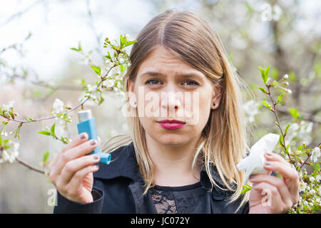 Picture of a young woman having pollen allergy, holding a bronchodilator outdoor Stock Photo