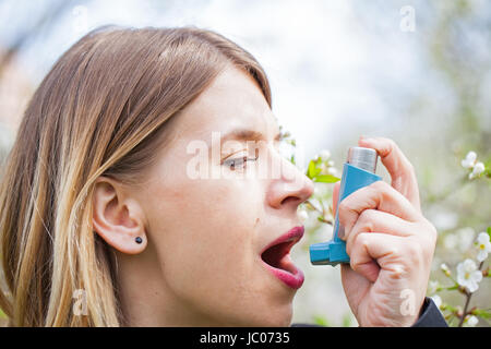 Picture of a young woman having pollen allergy, holding a bronchodilator outdoor Stock Photo