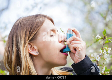 Picture of a young woman having pollen allergy, holding a bronchodilator outdoor Stock Photo