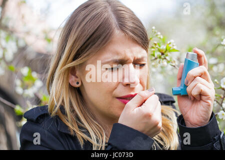 Picture of a young woman having pollen allergy, holding a bronchodilator outdoor Stock Photo