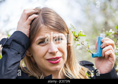 Picture of a young woman having pollen allergy, holding a bronchodilator outdoor Stock Photo