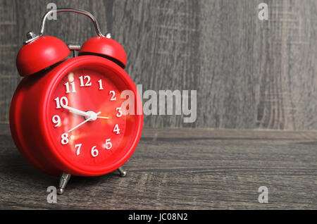 Old style red clock on a wooden background with space for text next. Stock Photo