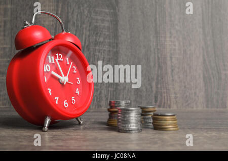 Time is money concept: Old style red clock with some money around on a wooden background with space for text to the side. Stock Photo