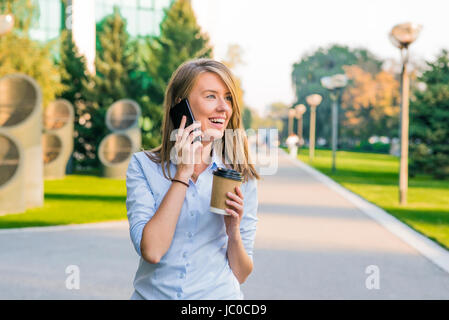 Young Woman with smartphone walking on street, downtown. In background is blurred street, looking in front Stock Photo