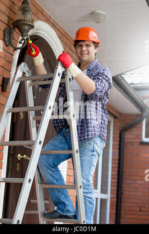 Young smiling electrician in hardhat climbing the stepladder Stock Photo