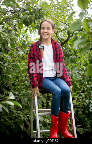 Happy young girl in red wellington boots  sitting on stepladder at garden Stock Photo
