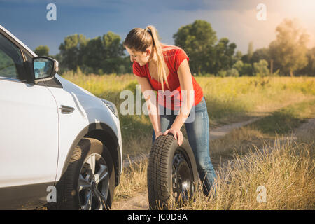 Beautiful young woman rolling spare tire to change the flat one Stock Photo
