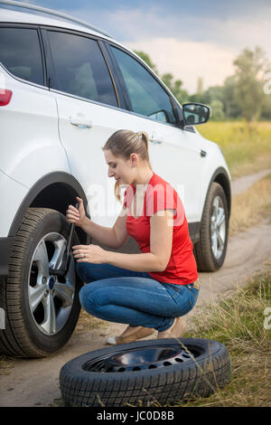 Young woman unscrewing nuts on car flat wheel at field Stock Photo