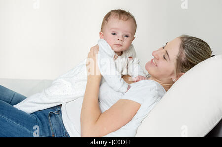 Portrait of happy young mother lying on bed and holding her 3 months old baby boy Stock Photo