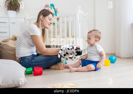 Beautiful young mother and her 10 months old baby son playing with puppets on floor at living room Stock Photo