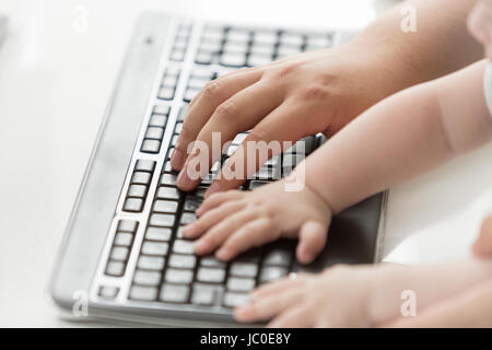 Closeup photo of father teaching his baby how to use computer keyboard. Concept of communications between generations Stock Photo