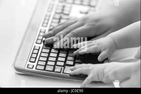 Black and white conceptual shot of adult and baby hands on computer keyboard Stock Photo
