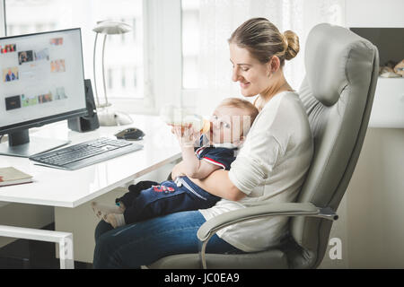 Portrait of young self employed mother working at home and taking care of her baby Stock Photo