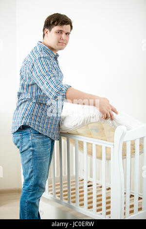 Young expectant father putting mattress in baby's cot at nursery Stock Photo