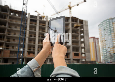 Closeup image of young woman posing on building site and using digital tablet Stock Photo
