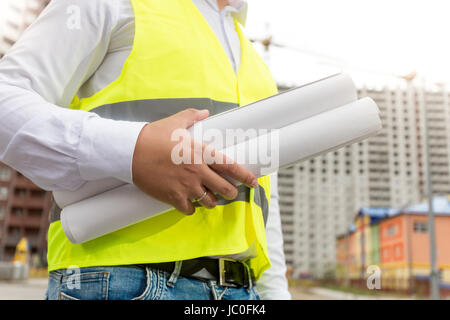 Closeup photo of engineer in safety vest holding rolled blueprints Stock Photo