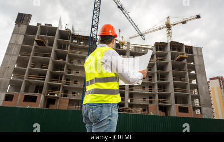 Young engineer on building site checking plans and blueprints Stock Photo