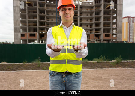 Portrait of young engineer standing against building site and holding digital tablet. Perfect for placing your image on tablet Stock Photo