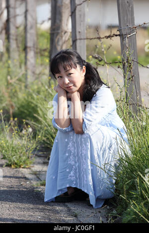 sad young woman posing alone sitting near barbed wire fence Stock Photo