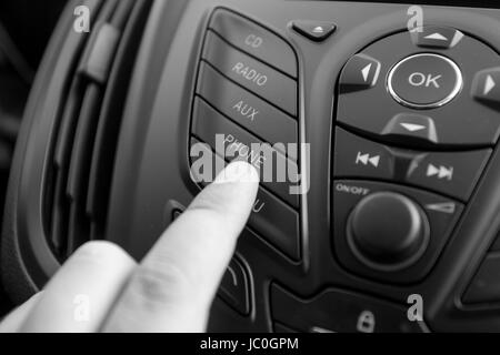 Black and white closeup photo of driver pushing radio button on dashboard Stock Photo