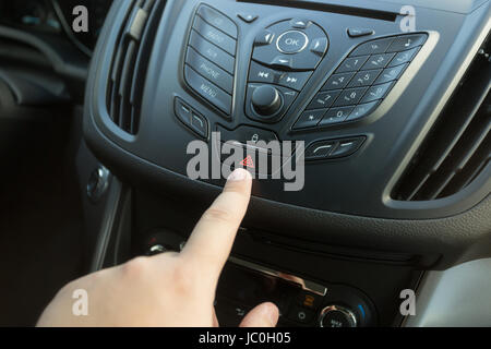 Closeup photo of driver pressing emergency button on car dashboard Stock Photo