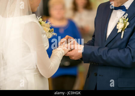 Closeup of young groom putting wedding ring on bride's finger Stock Photo