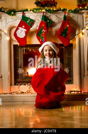 Cute little girl sitting in Santa red bag at fireplace Stock Photo